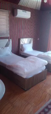 two beds in a bedroom with a red wall at Wadi Rum Sand moon Camp &Tour in Wadi Rum