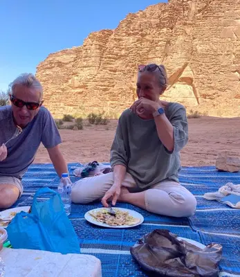 a man and woman sitting on a blanket with a plate of food at Sands of time desert camp in Wadi Rum