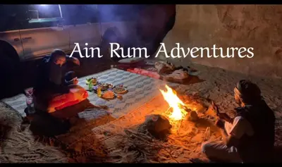 two people sitting around a fire with the words aim run adventures at مغامرات عين رم in Wadi Rum