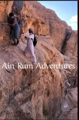 two people are climbing up a rocky mountain at مغامرات عين رم in Wadi Rum