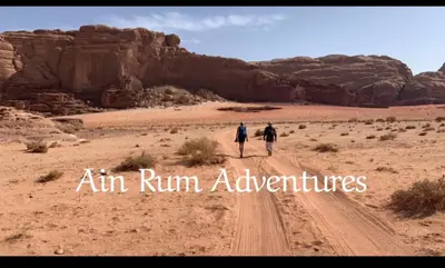 two people walking down a dirt road in the desert at مغامرات عين رم in Wadi Rum