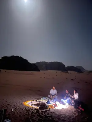 three people sitting around a fire on the beach at Bedouin Luxury Camp in Wadi Rum