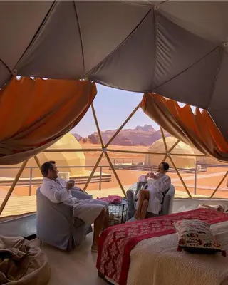 three men sitting in chairs in a tent with a view at RUM FLORAA LUXURY CAMp in Wadi Rum