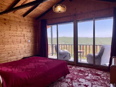 a bedroom with a bed and two chairs and a large window at كوخ واستراحة شيخ الجبل in Ajloun