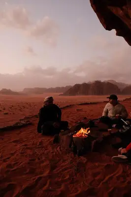 a group of people sitting around a fire on the beach at Wadi Rum Desert Experience in Wadi Rum
