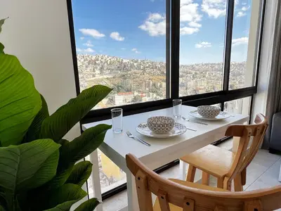 a white table with two chairs and a large window at Central Amman Stunning Views Apt in Amman