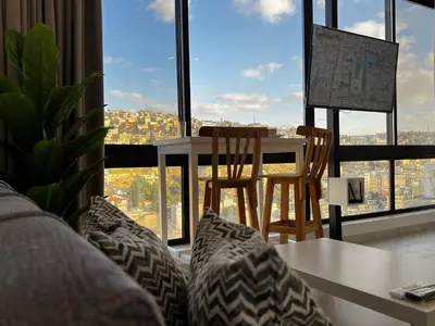 a living room with a table and chairs in front of a window at Modern Studio Apartment Near Downtown, breathtaking view! in Amman