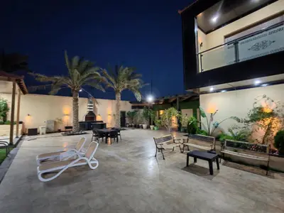 a patio with chairs and tables and palm trees at night at Wonder Villa in Al Rama