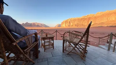 a person sitting in a chair on a patio looking at the desert at Wadi Rum Camp and Tours in Wadi Rum