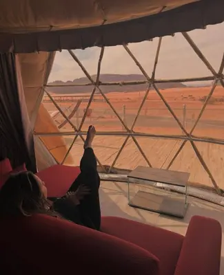 a person sitting on a couch looking out of a window at a desert at wadi rum luxury bubble soul in Wadi Rum