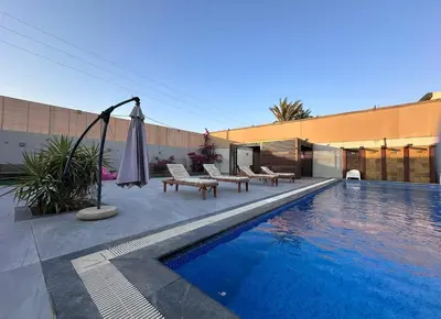 a swimming pool with an umbrella and benches next to a building at SunValley in Al Rama