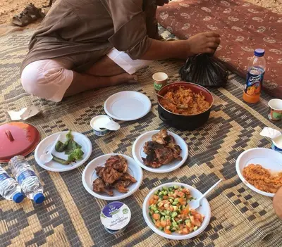 a person sitting on the floor with plates of food at Adventure Nights Camp in Wadi Rum