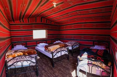 a room with three beds in a red room at Adventure Nights Camp in Wadi Rum