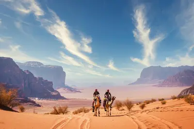 two people are riding horses in the desert at مخيم نجوم رم in Maḩaţţat Dīsah