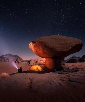 a person sitting on a rock under a mushroom in the desert at مخيم نجوم رم in Maḩaţţat Dīsah