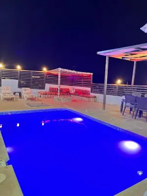 a blue swimming pool at night with chairs and umbrellas at شاليه بانا جرش in Jerash