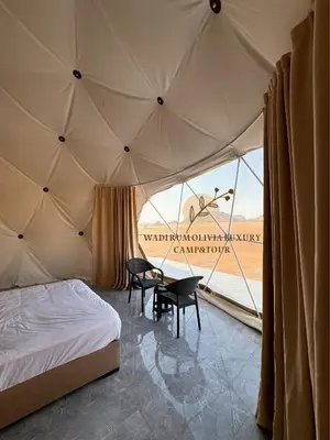 a bedroom with a bed and a table in a tent at WADI RUM OLIVIA lUXURY CAMP & TOUR in Wadi Rum