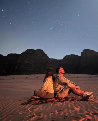 a man and woman sitting on the desert under the stars at saleem with jeep tour in Wadi Rum