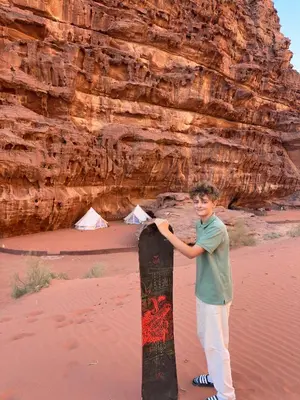 a young man holding a skateboard in the desert at The Legacy of Wadi Rum in Wadi Rum