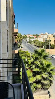 a balcony of a building with palm trees and a street at Loom & Light In the best location in Abdoun Amman in Amman