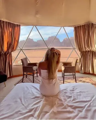 a woman sitting on a bed looking out of a window at RUM MAGIC BUBBLE lUXURY CAMP in Wadi Rum