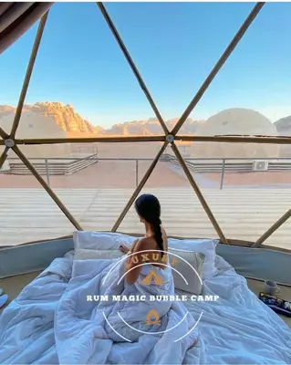 a woman sitting on a bed looking out of a window at RUM MAGIC BUBBLE lUXURY CAMP in Wadi Rum