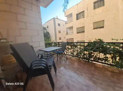 a balcony with chairs and a table and a building at شقة مميزة in Rujm Maghghijhah