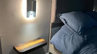 a light next to a bed with a pillow at T Cozy Chalet in Ash Shāghūr