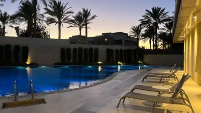 a pool with chairs and palm trees at night at Flow - Al Raha Village in Aqaba