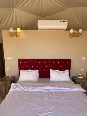 a bed with a red headboard and a air conditioner above it at Aurora Luxury Wadi Rum in Wadi Rum