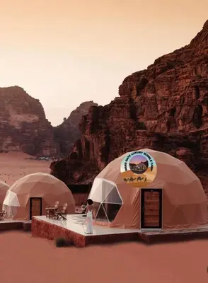 a person standing in front of three tents in the desert at MARS GATE lUXURY BUBBLE CAMP in Wadi Rum