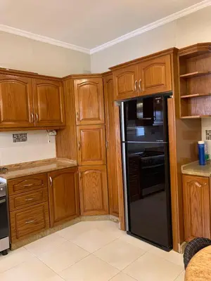 a kitchen with wooden cabinets and a black refrigerator at Shmeisani Cozy Apartment in Amman