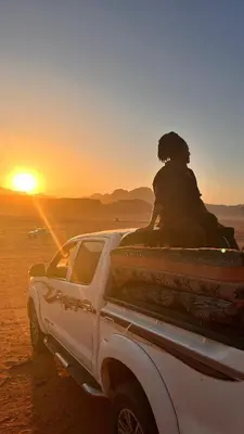 a person sitting on the back of a white truck in the desert at wadi rum planet camp in Disah