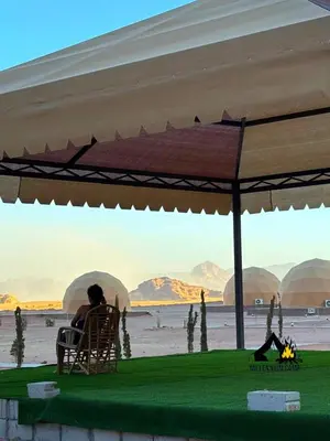 a person sitting in a chair under an umbrella on the beach at millennium camp in Wadi Rum