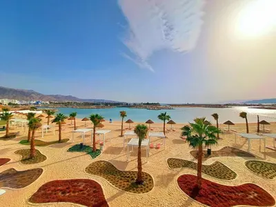 a beach with palm trees and umbrellas and a body of water at واحة ايلة ازور in Aqaba