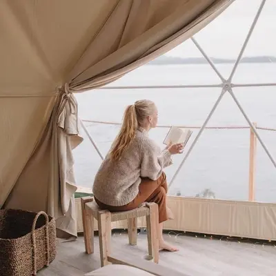 a woman sitting on a stool reading a book in a tent at Rum marea in Disah