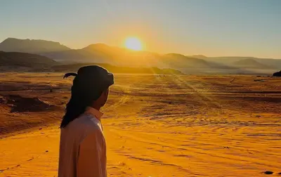 a woman standing in the desert watching the sunset at Starlight Camp in Disah