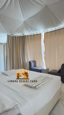 a white bed in a tent with two chairs at Lunara Desert Luxury Camp in Wadi Rum
