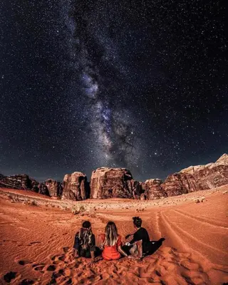three people sitting in the desert under the stars at ROYAL SAVOY lUXURY CAMP in Wadi Rum