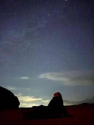 a person sitting on the ground looking up at the night sky at Rum Desert Silence Camp in Wadi Rum