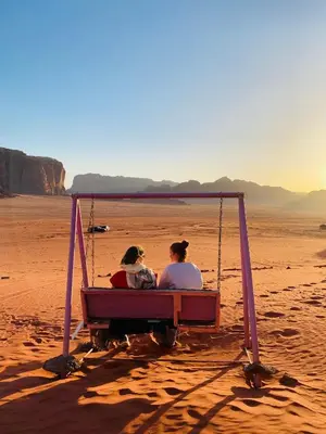 two women sitting on a swing in the desert at Rum Tale Camp in Wadi Rum