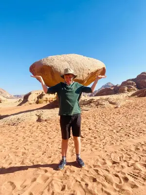 a man holding up a large rock in the desert at Rum Tale Camp in Wadi Rum