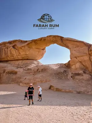 a group of people walking on the beach in front of an arch at FARAH RUM LUXURY CAMP & Bubbles Hotel in Wadi Rum