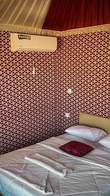 a bed in a room with a red wall at Wadi Rum Sila Camp in Wadi Rum