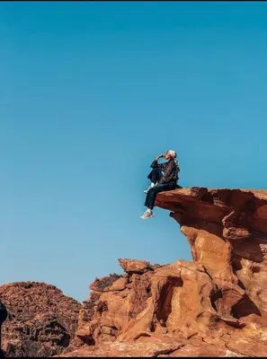 a person sitting on the side of a cliff at Eileen wadi rum camp in Wadi Rum