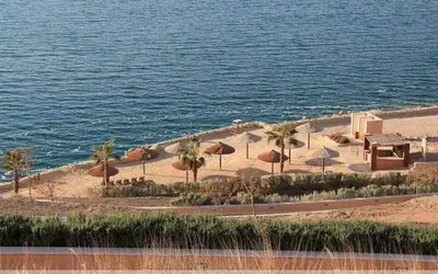 a beach with umbrellas and palm trees and the water at Family WeekEnds Getaways at Samarah Resort Studio in Sowayma