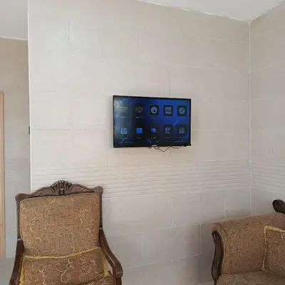 a tv hanging on a wall with a chair at ابو عبدالله للشقق الفندقيه in Ajloun