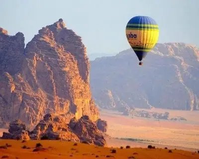 a hot air balloon flying over a desert with mountains at Wadi Rum in Al Jafr