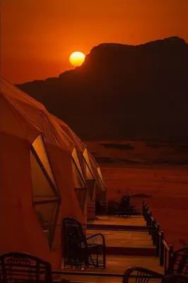 a sunset on the beach with chairs and a tent at RUM AlLIRA lUXURY CAMP in Wadi Rum