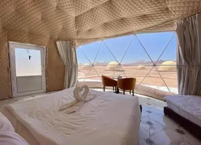 a bedroom with a bed and chairs and a large window at Moon Red Bubbles Camp in Wadi Rum